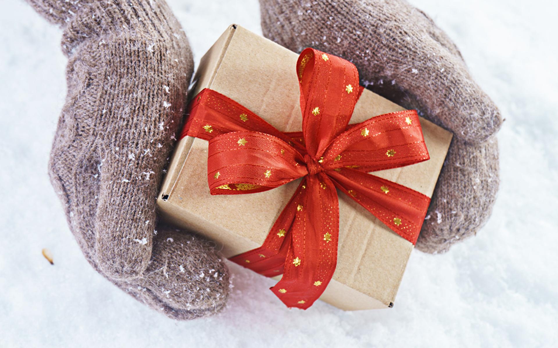 Hände in Handschuhen halten ein Geschenk