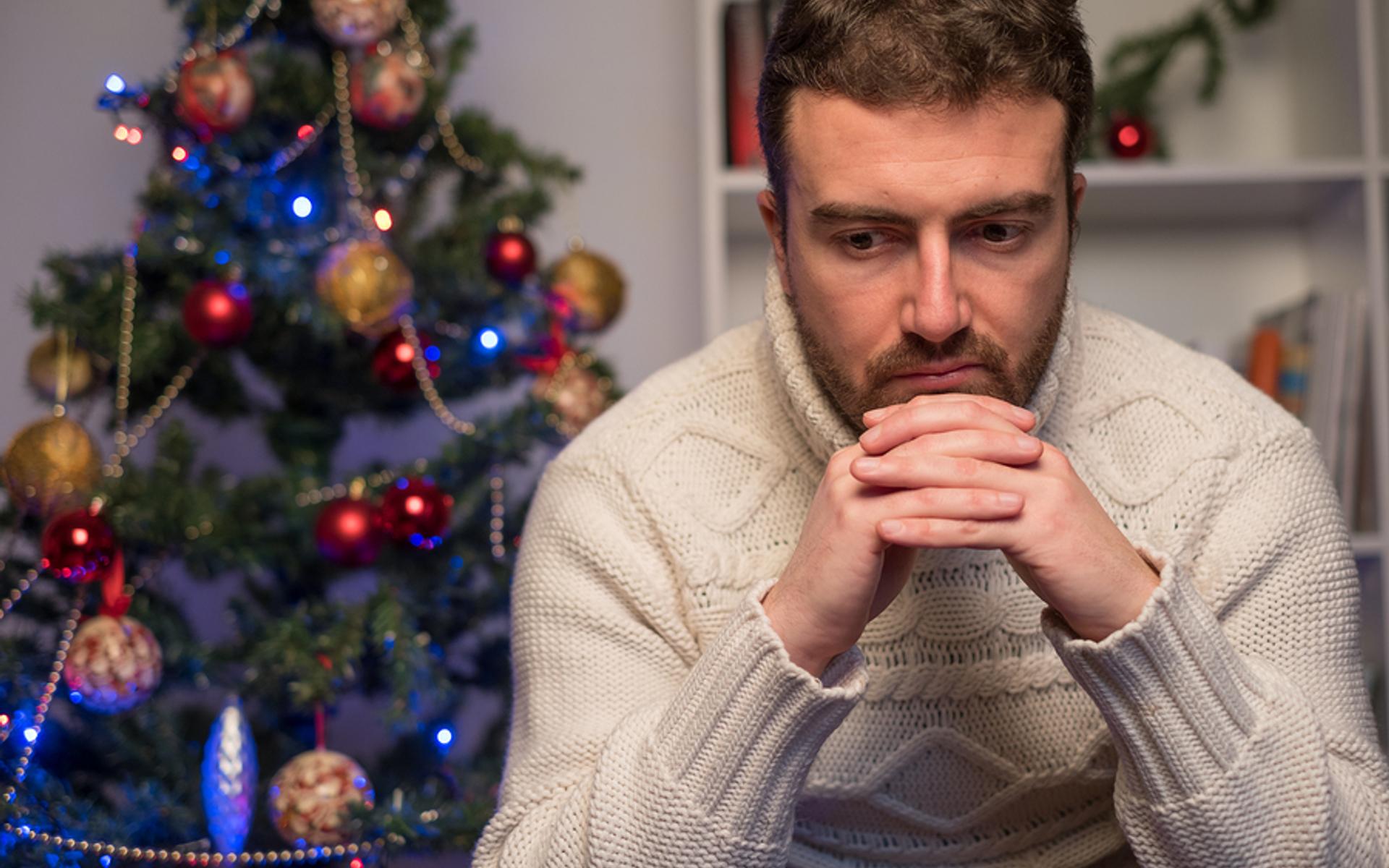 Deprimierter Mann vor Weihnachtsbaum