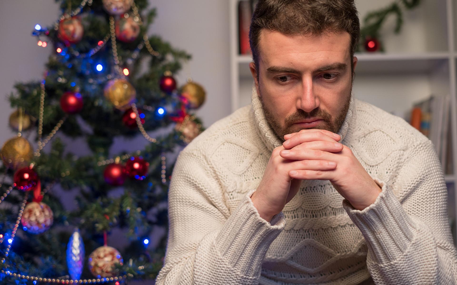Deprimierter Mann vor Weihnachtsbaum