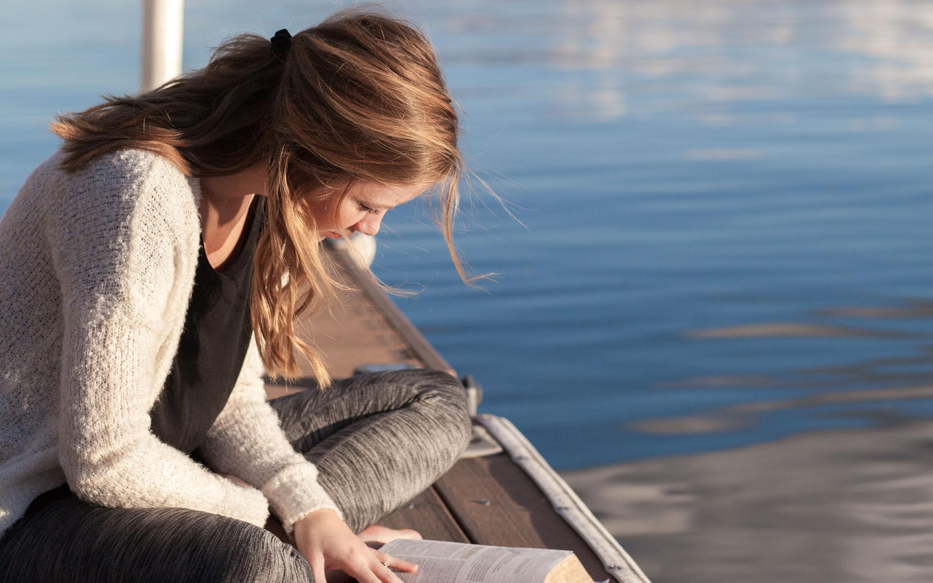 Ein Mädchen liest Bibel am See