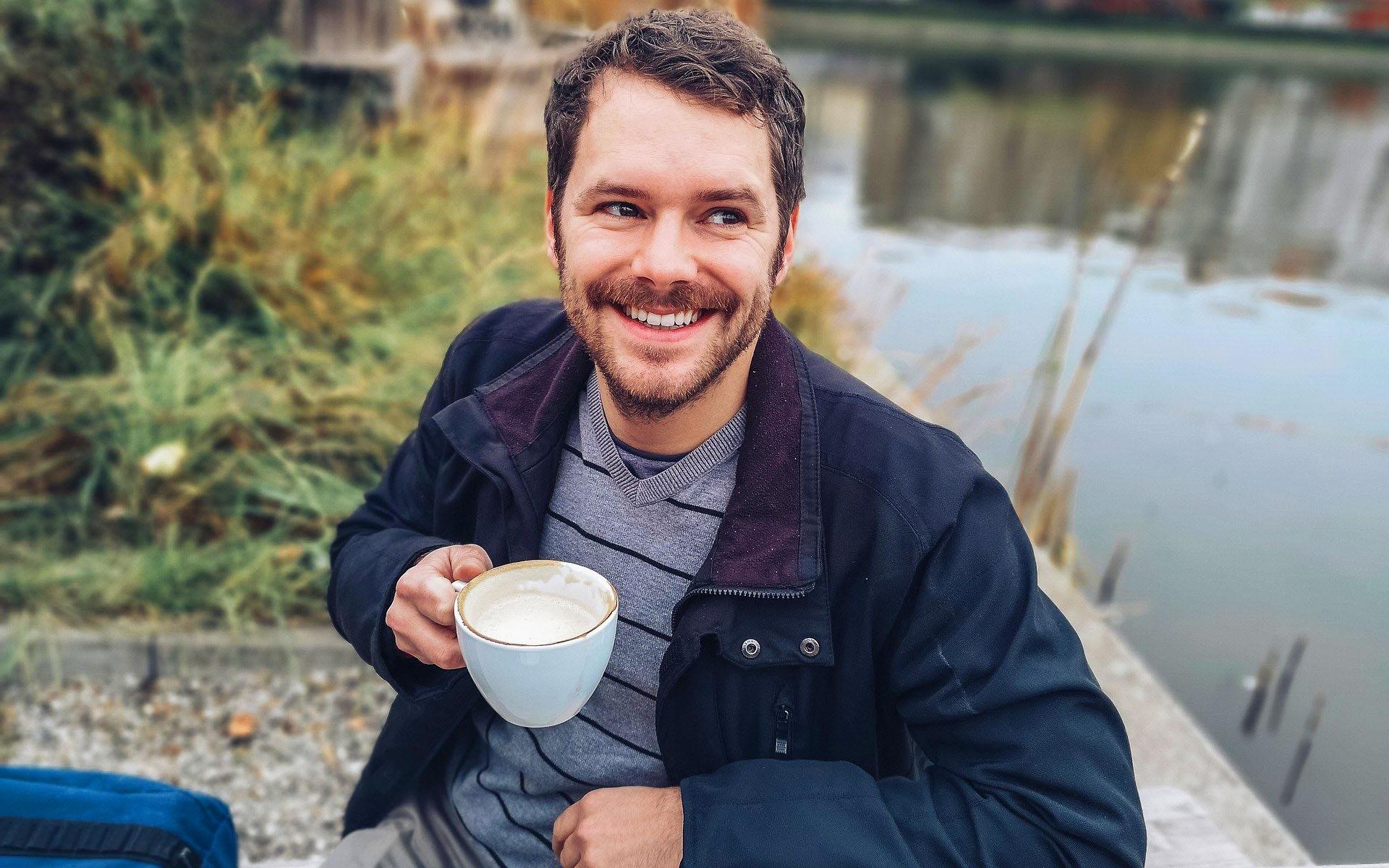 Mann trinkt einen Kaffee und lächelt dabei