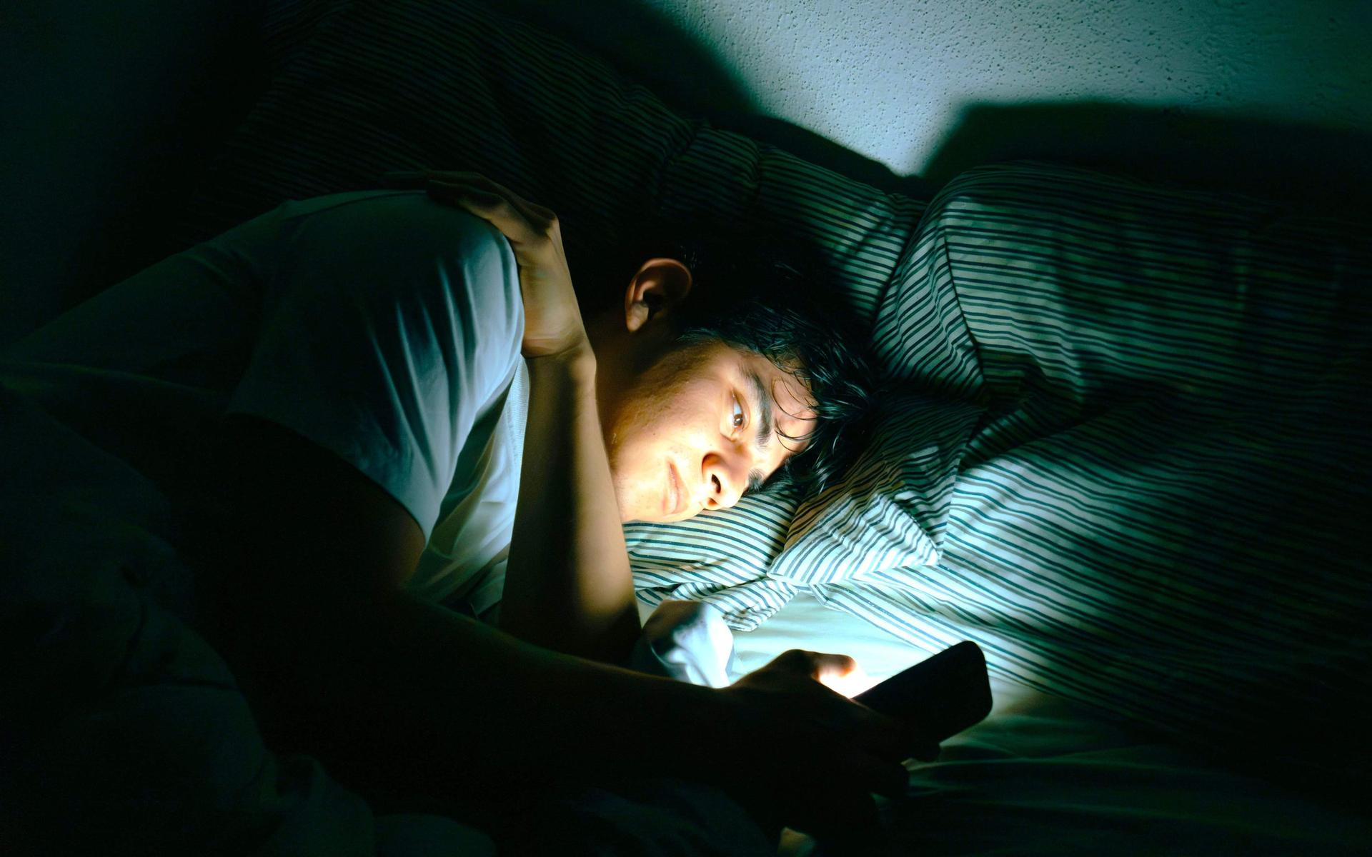 person-im-bett-die-auf-einen-leuchtenden-handybildschirm-schaut
