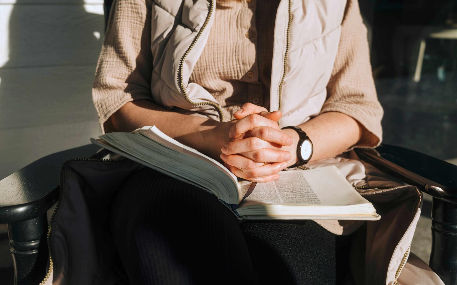 Frau faltet die Hände über die Bibel