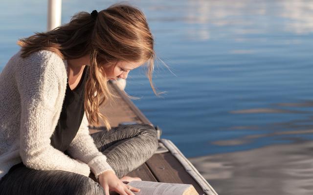Ein Mädchen liest Bibel am See