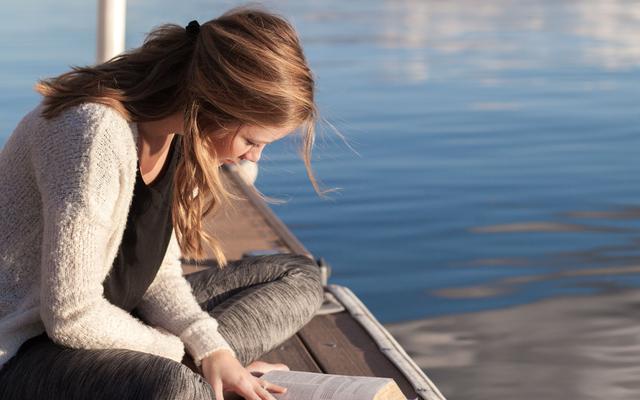 Ein Mädchen liest Bibel am See
