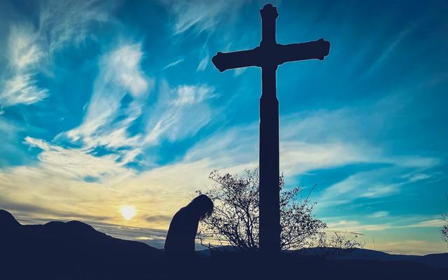 Frau kniet vor einem Kreuz