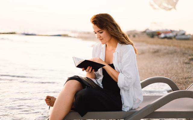 Frau liest die Bibel am Strand