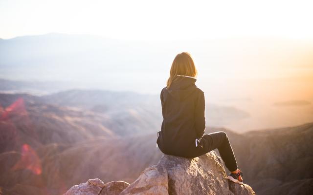 Junge Frau sitzt alleine auf einem Berg