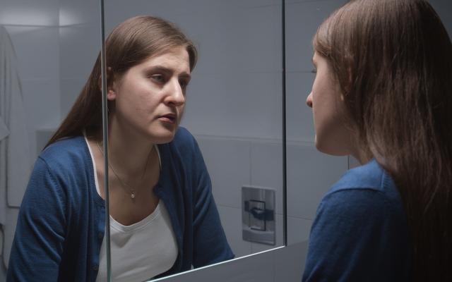 Verunsicherte Frau die sich im Spiegel anschaut
