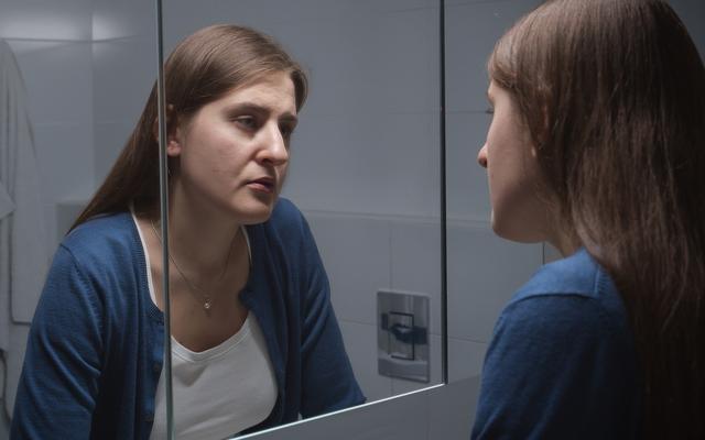 Verunsicherte Frau die sich im Spiegel anschaut