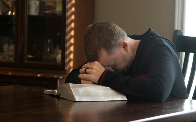 Ein Mann betet am Tisch mit seiner Bibel