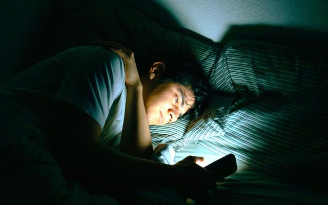 person-im-bett-die-auf-einen-leuchtenden-handybildschirm-schaut