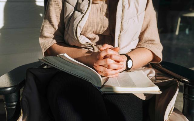 Frau faltet die Hände über die Bibel